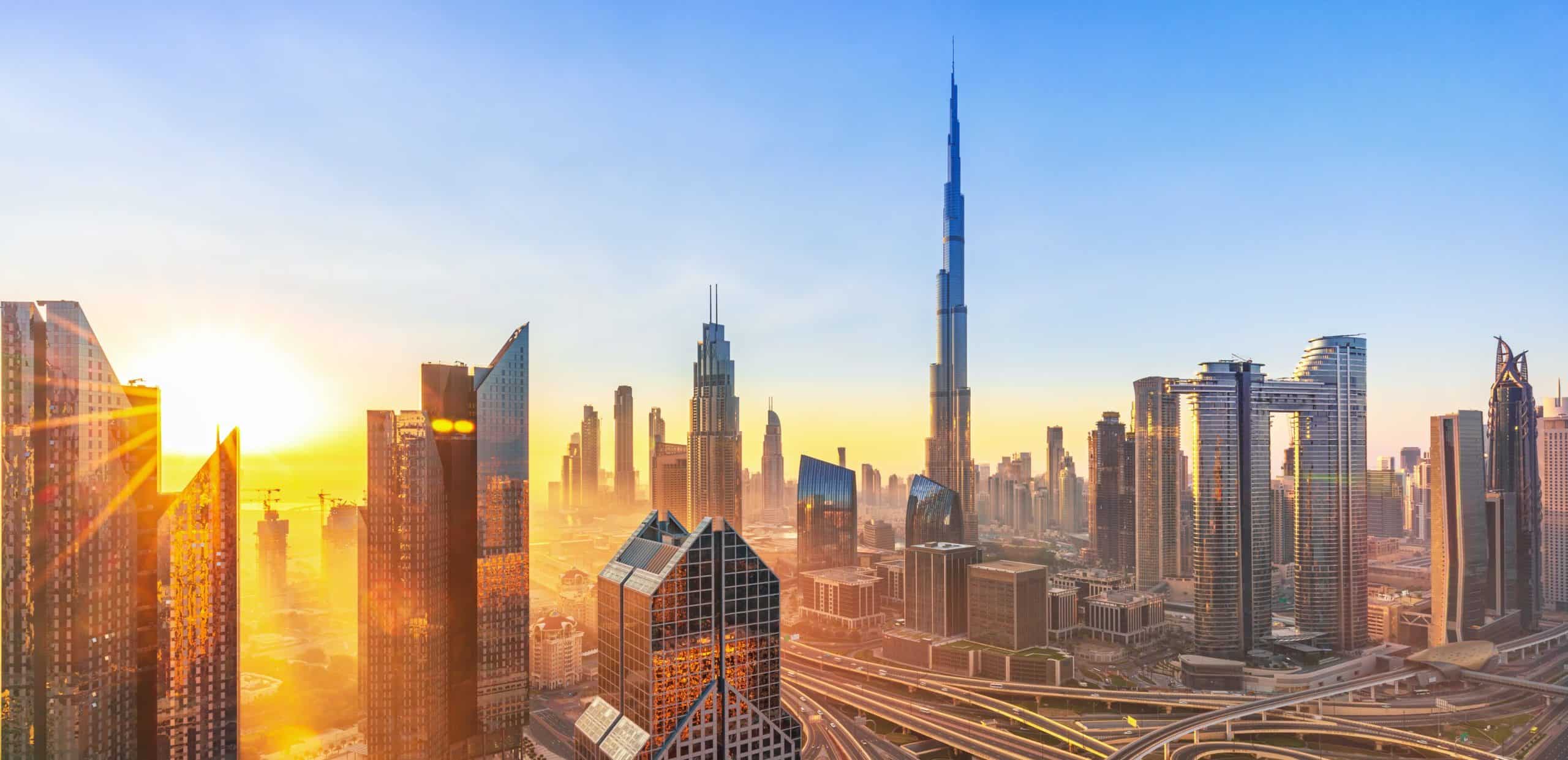 Sunrise over a skyline with needle tower, clear golden sky, modern skyscrapers, and intricate highways.