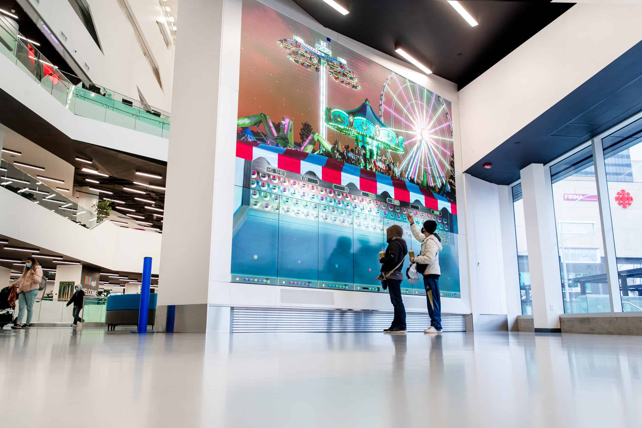 Two people admire a colorful carnival display with a ferris wheel in a modern building with glass railings.